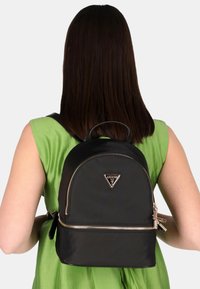 Zaino in nylon nero dalla forma arrotondata, con cerniera argentata e logo triangolare. Il design presenta una maniglia superiore e spallacci regolabili.