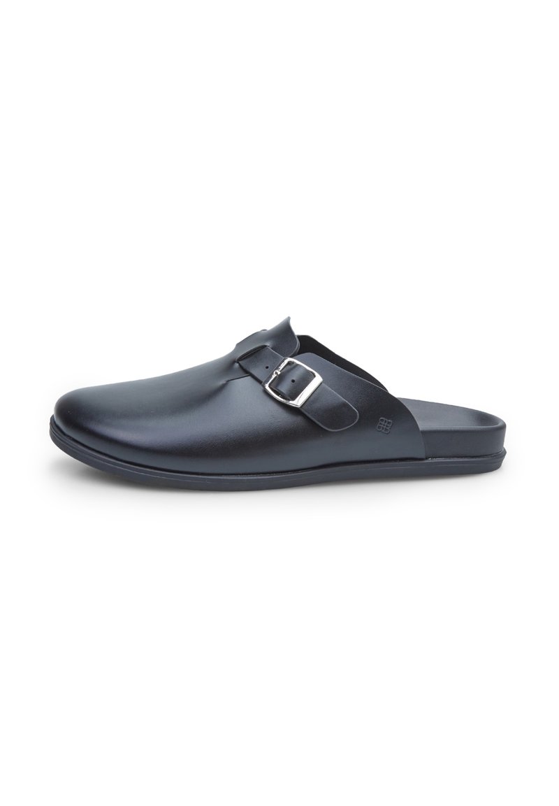 Fekete szintetikus slip-on klumpa lekerekített orral, állítható ezüst csattal és texturált felsőrésszel, lapos talppal.