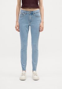 Svetlomodré úzke džínsy s vysokým pásom, prednými vreckami a svetlým umývaním. Kombinované s bielymi teniskami. Hladká textúra denimu.