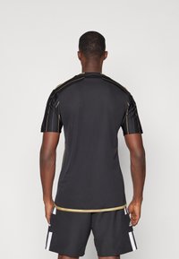 Maglietta sportiva nera con maniche corte, caratterizzata da cuciture dorate lungo le spalle e il collo. Tessuto liscio e leggero.