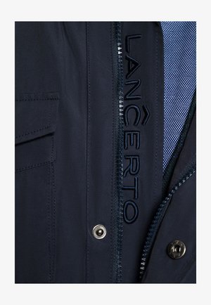 Marynarka w kolorze granatowym z zapięciem na zamek błyskawiczny, widocznym haftowanym logo, teksturowanym materiałem oraz detalami z zatrzaskami. Podszewka z wzorzystej tkaniny.