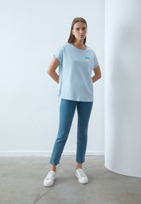 Lyseblå t-shirt i blødt stof med afslappet pasform og opret rullede ærmer, parret med slim-fit blå jeans og hvide sneakers.