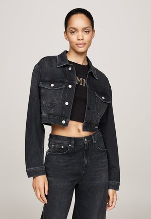 Chaqueta de mezclilla negra recortada con cierre de botones, dos bolsillos en el pecho, herrajes plateados, combinada con jeans negros de cintura alta con una textura sutil.