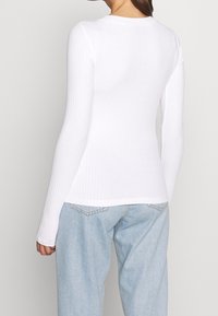 Witte ribgebreide lange mouwen top met een ronde halslijn, voorzien van een getailleerd silhouet en zachte textuur. Gecombineerd met lichtblauwe denim jeans.