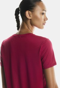 Rdeča športna majica s kratkimi rokavi in okroglo ovratnikom, ki se ponaša z gladko teksturo in lahkotnim materialom, prikazana s hrbtne strani.