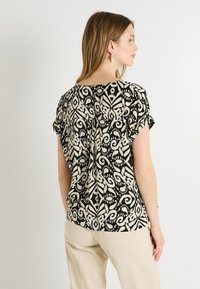Top de patrones en negro y marfil con mangas cortas, que presenta un diseño floral y un corte relajado, confeccionado en tela ligera.