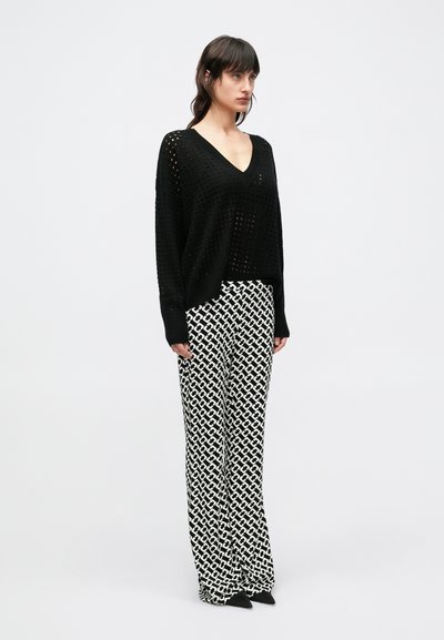 Mustast kudumist kampsun V-kaelusega ja suurte avatud silmustega. Sobitatud laia säärega pükstega, millel on musta ja valge geomeetrilise mustriga.