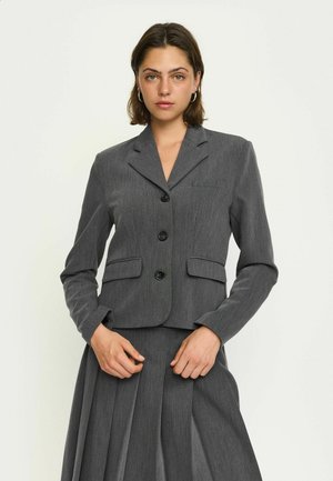 Šedý blazer s přiléhavým střihem, má klopový límec, tři knoflíky a boční kapsy. Materiál má jemnou strukturu a pruhovaný vzor.
