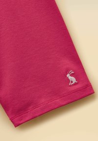 Růžový látkový rukáv s malým bílým vyšívaným zajíčkem u lemu na světle béžovém pozadí.