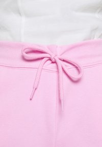 Růžové tepláky s texturovanou tkaninou, vybavené stahovací šňůrkou a hladkým pasem. Doplňky zahrnují lemované švy.