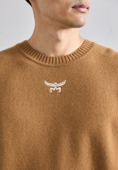 Pruun sooniku särk ribidega ümar kaelus. Rinnaosale on tikandina kujutatud valget logo. Pehme tekstuur.