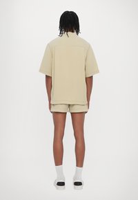 Chemise beige oversize à manches courtes associée à un short assorti, fabriquée en tissu doux. Design simple avec ourlet droit, vue de dos.