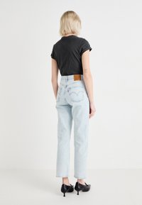 Camiseta negra de manga corta combinada con unos vaqueros de tiro alto en un tono azul claro, que presentan un parche de cuero marrón y un corte recto. Tacones negros de punta.