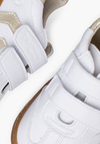 Baskets synthétiques blanches avec accents beiges, deux bandes Velcro, tige texturée, semelle en caoutchouc et bout rond.