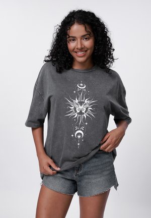 Gray oversized t-shirt in soft cotton with a white sun and butterfly graphic design on the front, paired with distressed denim shorts.