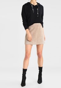 Sudadera negra con capucha y cordones estampados, combinada con una mini falda de ante beige y botas negras por encima de la rodilla. Textura suave, ajuste casual.