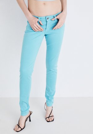 Jeans ajustados turquesa hechos de una mezcla de algodón, con cierre de botón y trabillas para el cinturón, combinados con tacones negros con tiras.