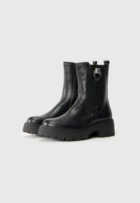 Botines de piel negra con suela de goma gruesa, cierre con cremallera y detalle de tira en el talón. Textura suave con costuras mínimas.