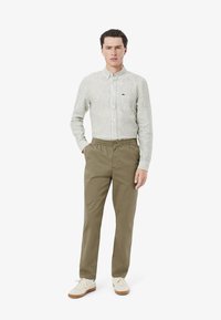 Gestreepte overhemd voor heren in wit en groen met lange mouwen, gecombineerd met olijfgroene broek met elastische taille en witte sneakers.