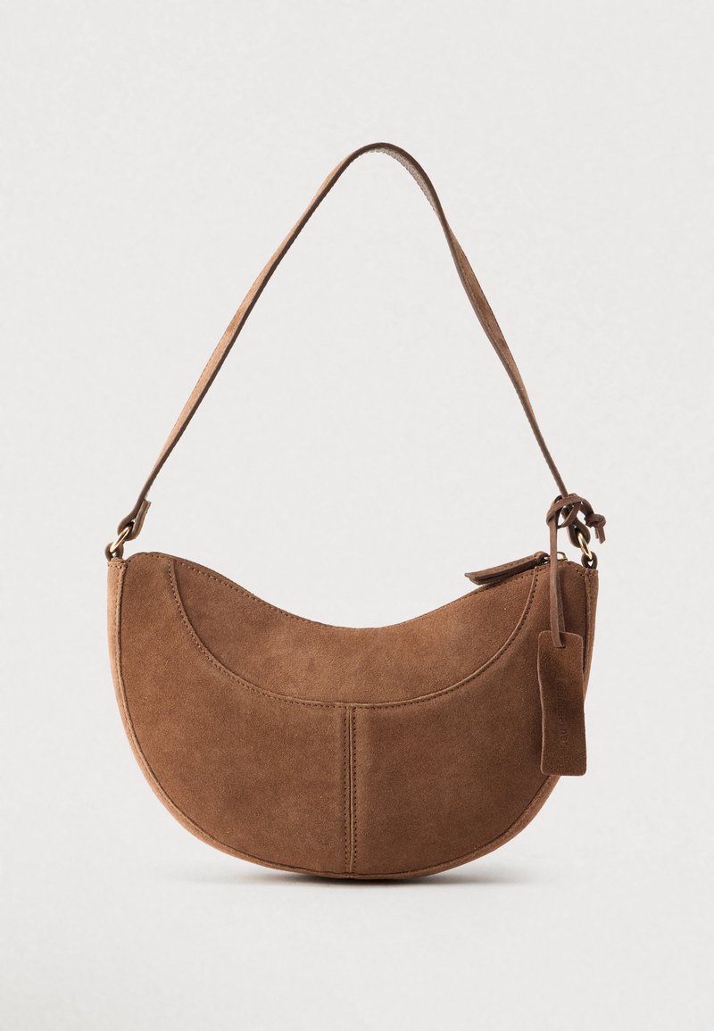Bruine suède handtas met een gebogen, halve maanvorm. Voorzien van een schouderriem, een klein label en zichtbare stiksels langs de randen.