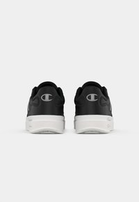 Zapatillas negras con parte superior texturizada, suela de goma blanca y sutil branding gris en el talón. Acabado suave con diseño redondeado.