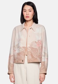 Cropped floral jacket in soft beige with gold snap buttons, featuring large pink and white flower designs on lightweight fabric.