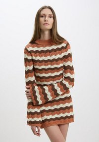 Maglione lavorato a maglia con maniche lunghe e svasate. Presenta un motivo ondulato nei colori ruggine, marrone e crema. Collo a coste e tessuto testurizzato.