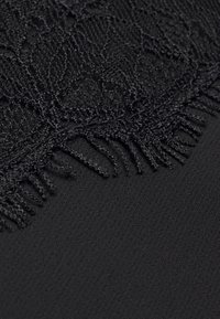 Gros plan sur un tissu noir avec une bordure en dentelle détaillée et une couture délicate de franges le long du bord.