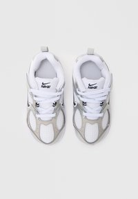Fehér hálós és ezüst szintetikus sportcipők fekete Nike logóval, fűzőkkel és szövet borításokkal. Átlátszó talp; lekerekített, párnázott design.