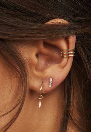 Goldene Creolen und Steckerohrringe mit klaren Edelsteinen. Die Creole hat einen hängenden Stab mit einem diamantähnlichen Design; der Stecker zeigt eine vertikale Linie von Steinen.