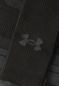 Μαύρες αθλητικές κάλτσες με ριμπ υφή και διακριτικό γκρι λογότυπο Under Armour στη μία πλευρά. Διακρίνεται ριγέ σχέδιο στο ύφασμα.