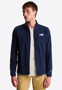 Chaqueta ligera azul marino con cremallera completa, bolsillo en el pecho con cremallera y logotipo en el pecho; textura suave, diseño práctico.