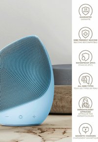 Appareil de nettoyage facial en silicone de couleur bleu clair avec surface texturée, forme courbée et boutons de fonctionnement. Comprend une fonction de charge magnétique.