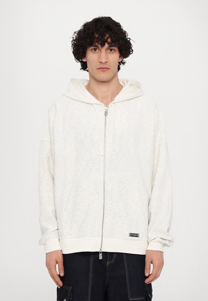 Haut de sweatshirt zippé blanc avec un motif texturé discret, doté d'une capuche avec cordon de serrage, de poignets et d'un ourlet côtelés. Étiquette de logo noire en bas.