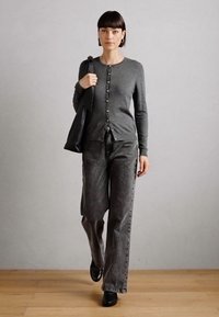 Gray knit cardigan with round buttons, paired with dark gray high-waisted pants. Black shoes and a black tote bag. Wood floor, neutral background.