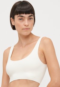 Hvit sømløs bralette med brede stropper og en glatt tekstur. Designet har minimalt med detaljer og en atletisk crop-silhuett.