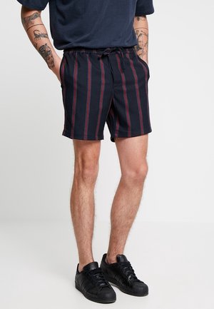 Pantalones cortos azul marino con prominentes rayas verticales rojas y blancas, cintura elástica con cordón y dos bolsillos laterales.