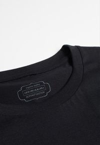 Límec černého trička z Supima bavlny s štítkem obsahujícím text "superior quality Intimissimi Supima Cotton." Hladká textura, jednoduchý design.