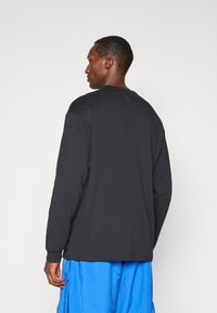 Schwarzes Langarmshirt aus weichem Material, Rundhalsausschnitt, mit lockerer Passform. Kombiniert mit blauen strukturierten Hosen, die eine glatte Rückansicht zeigen.