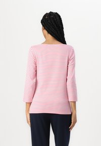Stripet rosa og hvit langermet topp med båtutringning. Mykt stoff, rett snitt, og trekvartlange ermer. Båret med mørke bukser.