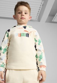Sudadera de color beige claro con patrones de siluetas coloridos en verde, azul, negro y coral, con el logo de "PUMA" en letras grandes en la parte delantera.