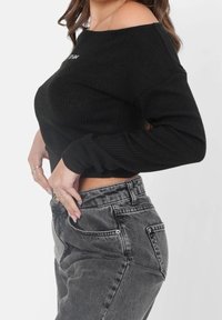 Mustavitsa ribattu cropped-neule off-shoulder-muotoilulla, yhdistettynä korkeavyötäröisiin haalistuneisiin harmaan värisiin farkkuihin, joissa on klassinen viiden taskun tyyli.