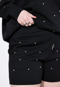 Pantaloni corti neri realizzati in un morbido tessuto, con piccole perle bianche sparse e una cintura elastica con lacci per una vestibilità regolabile.