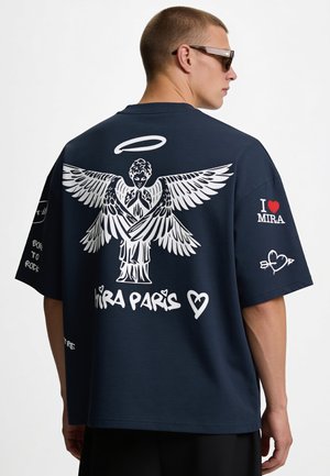 Homme portant un t-shirt oversize bleu marine avec un grand graphique d'ange blanc et le texte "MIRA PARIS" dans le dos, plus "I love MIRA" sur la manche.