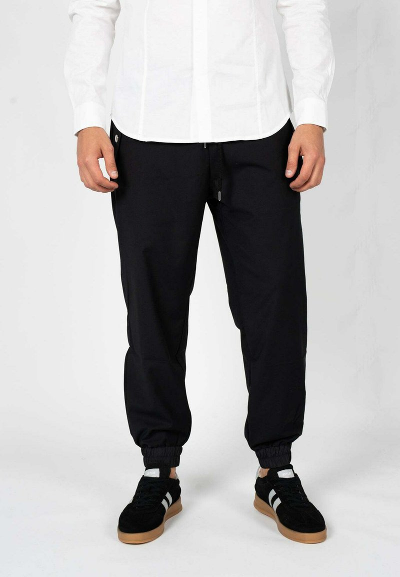 Zwarte joggingsbroek met elastische boorden, een trekkoord in de taille en zijzakken, gecombineerd met zwarte sneakers met witte strepen.