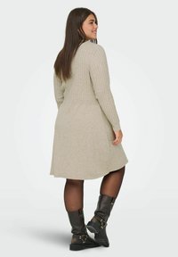Vestido de punto en beige claro con textura acanalada, cintura ajustada y falda acampanada, combinado con botas de cuero negras hasta la rodilla.