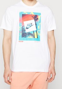 Valkoinen t-paita, jossa on värikäs auringonlasku ja palmun kuva, jossa on vinossa oleva valkoinen neliö, jossa on Nike-logo ja teksti "Just Do It."