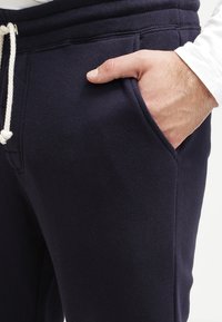 Marina blå sweatpants i mjukt material med dragsko i midjan, sidoficka och ribbade muddar. Slät yta utan synliga mönster.