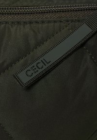 Mörkgrön tyg med en slät textur, med en svart dragkedja och en rektangulär gummimärke präglad med "CECIL."
