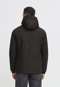 Black jacket with a hood, featuring a smooth exterior, elastic cuffs, and a streamlined design. No visible logos or patterns.